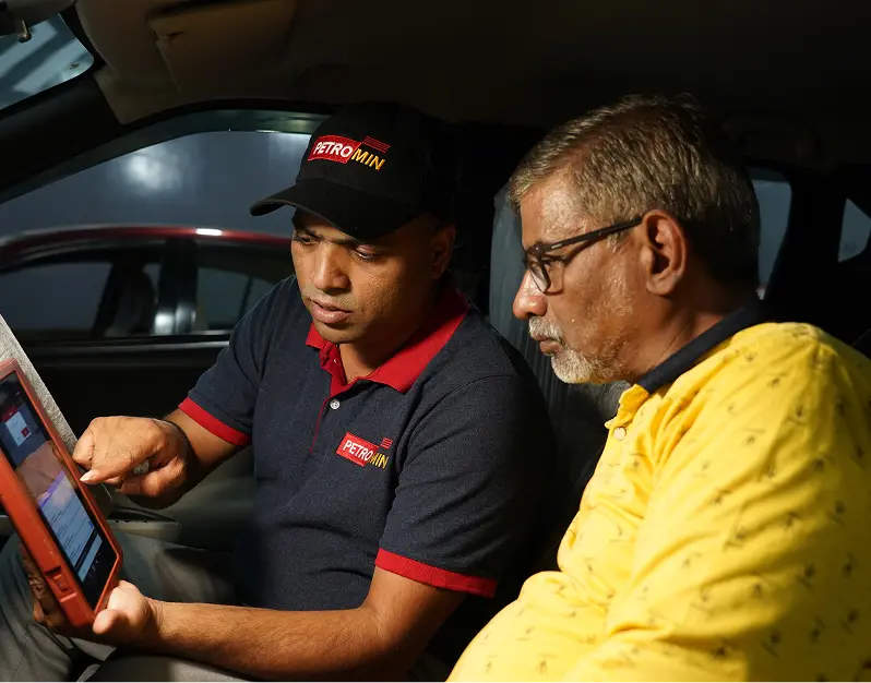 A Petromin Express employee sharing insights with a customer over a device, while being seated in a car.