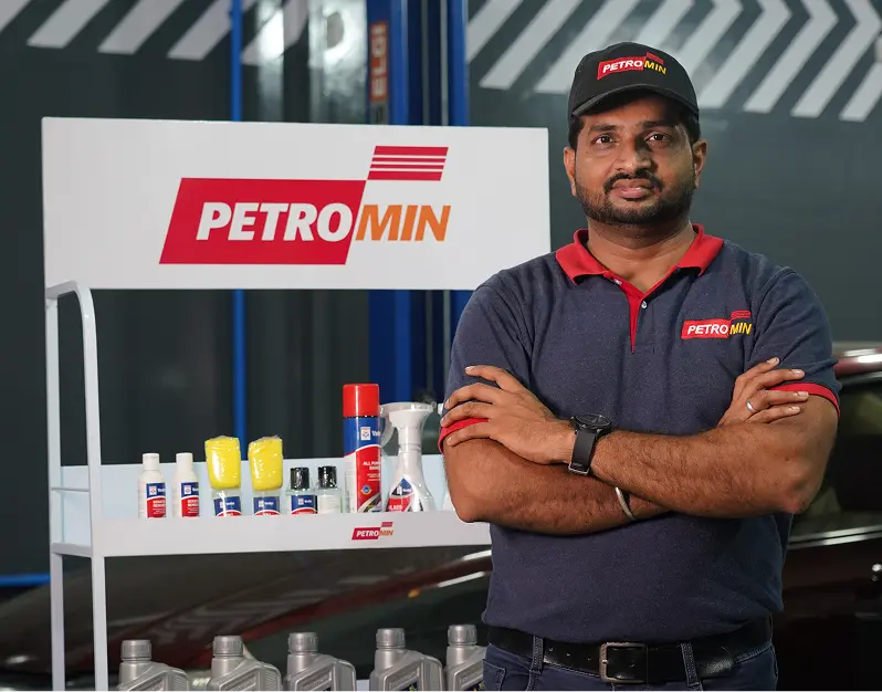 A Petromin Express employee standing with his hands crossed in front of a shelf with the brand's equipment and tools.